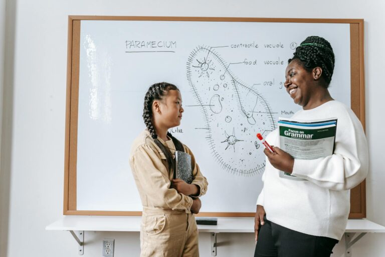 Side view of smiling African American female teacher holding textbooks while communicating with Asian teenage girl after lesson